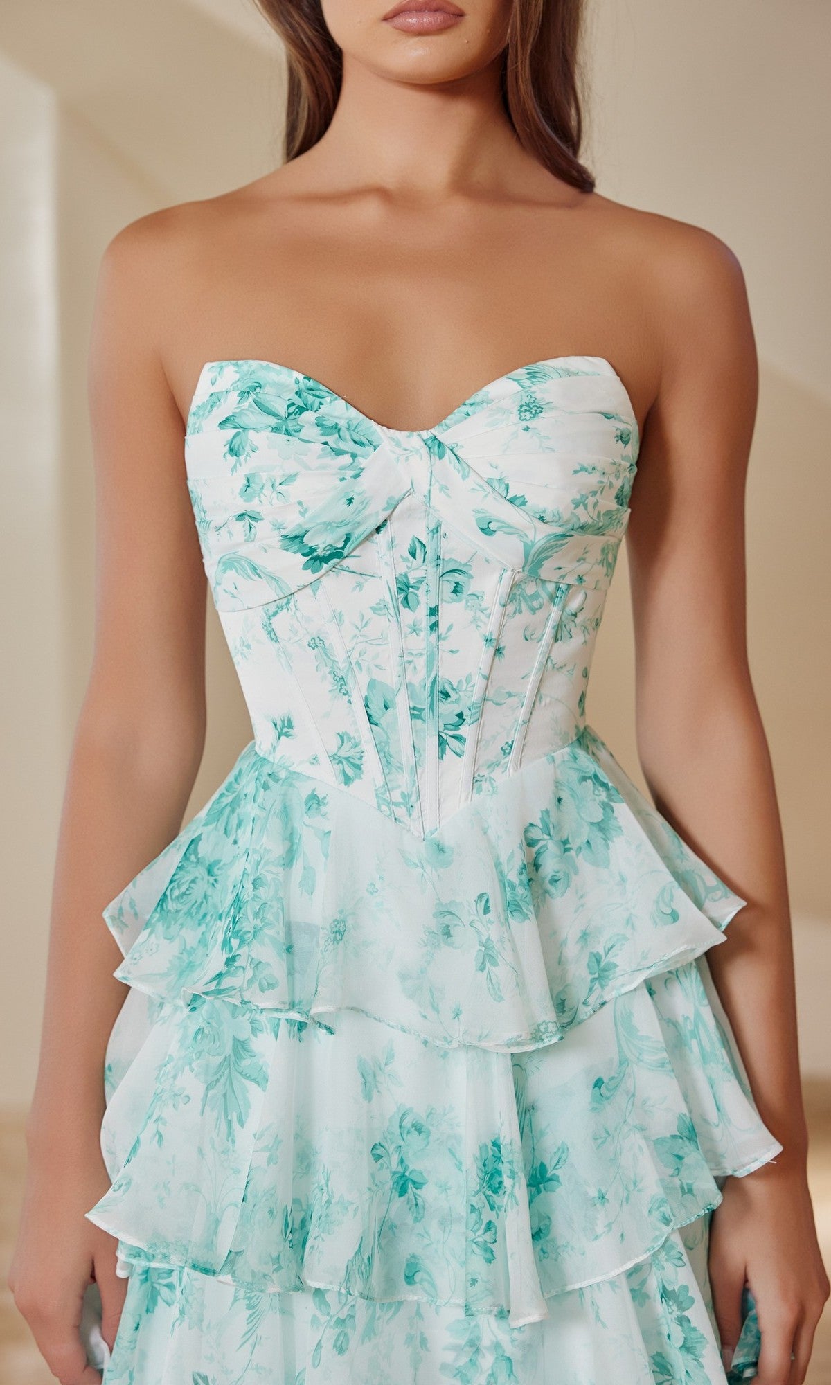 A woman wears the Nox Anabel T1865 Long Prom Dress, featuring a strapless floral chiffon design with a boned corset bodice and light blue A-line ruffle skirt.